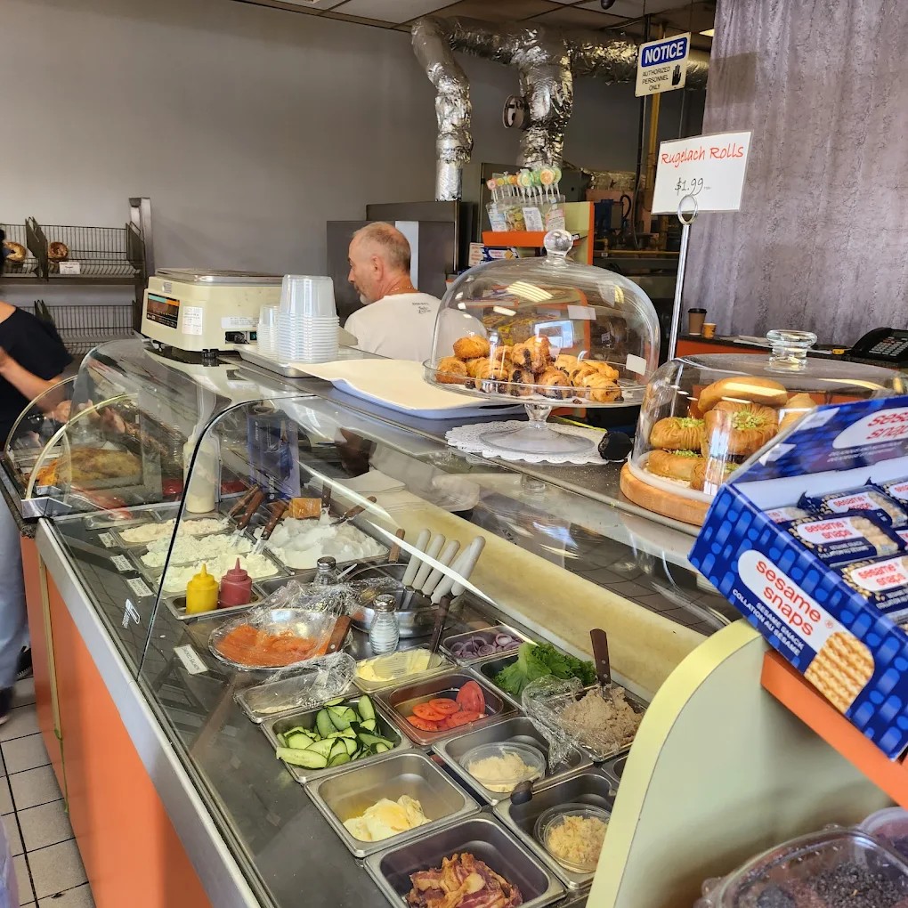Deli counter with curved glass case of toppings: lox, cream cheese, vegetables, and condiments.